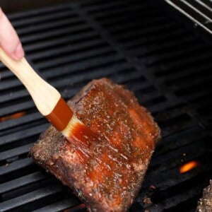 Brushing barbecue sauce onto sous vide ribs on a barbecue grill.