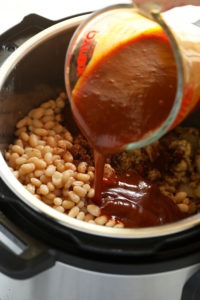 A person seasoning Instant Pot baked beans with sauce.