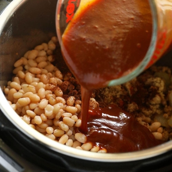 A person seasoning Instant Pot baked beans with sauce.