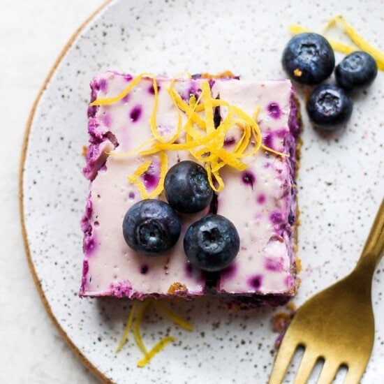 blueberry cheesecake bar on a plate topped with fresh berries.