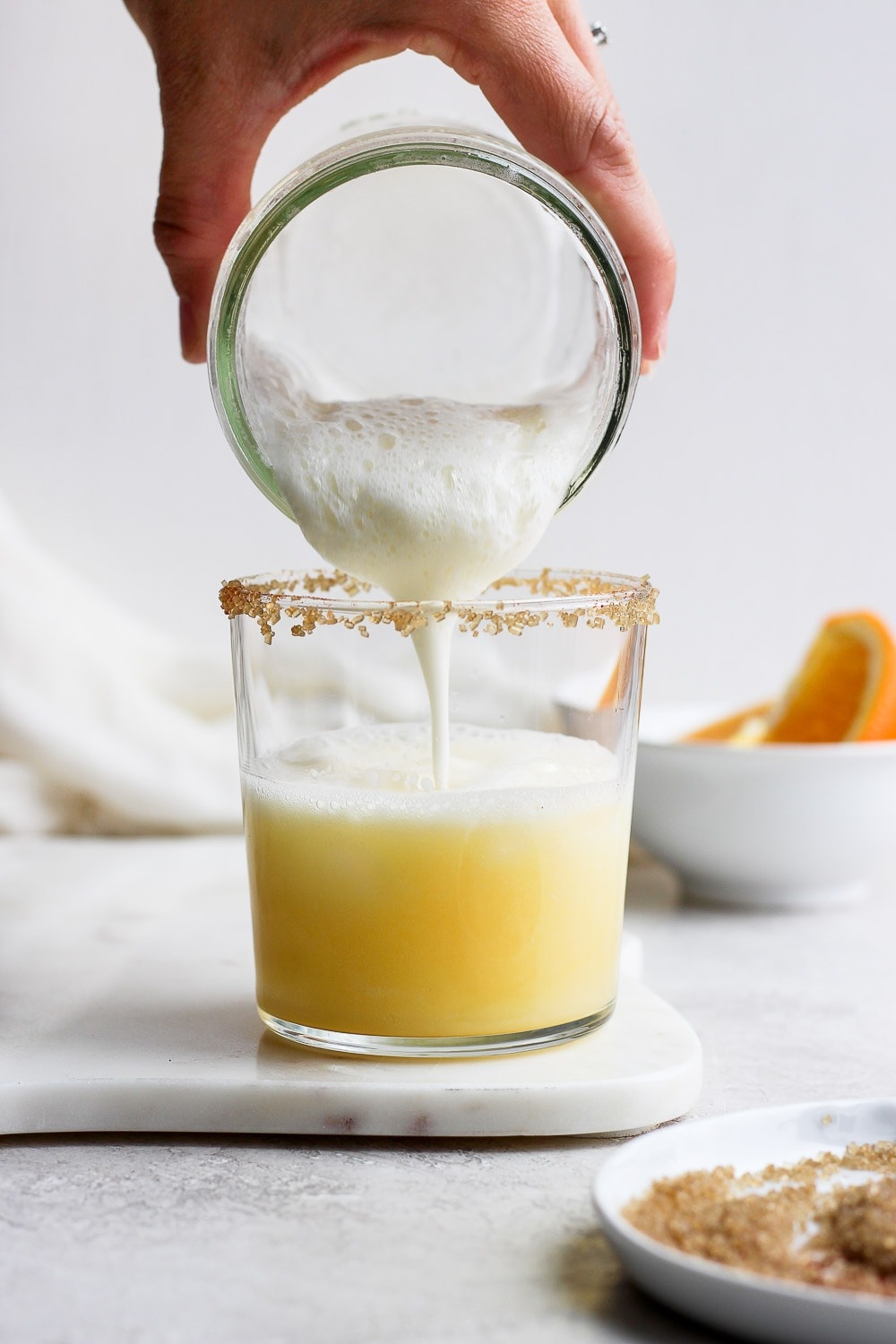 Pouring froth into an orange cocktail.