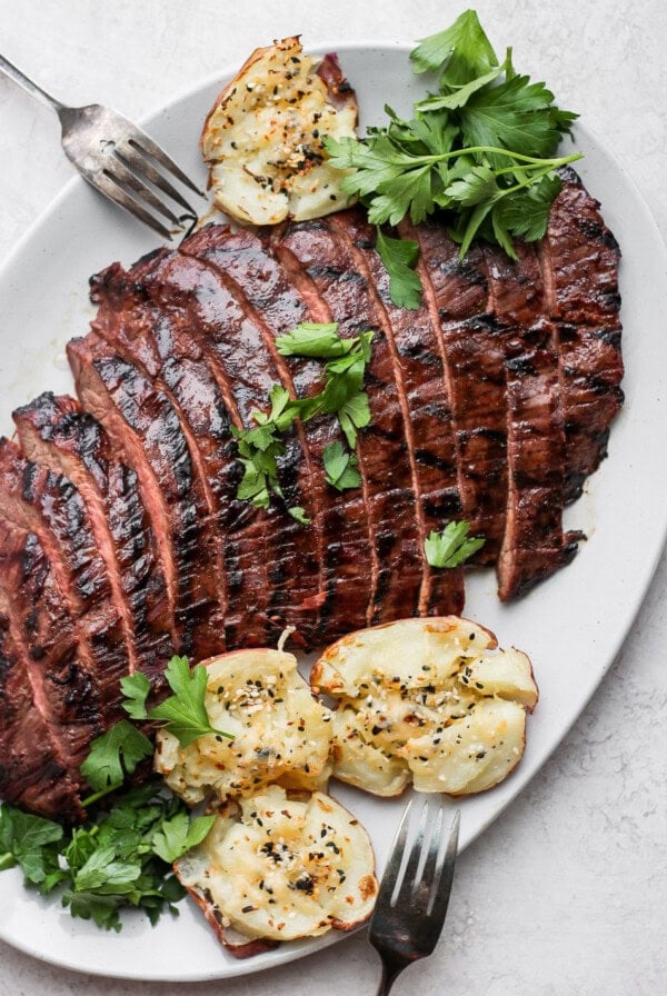 Grilled flank steak on a plate with potatoes.