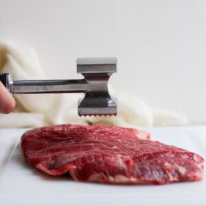 tenderizing flank steak on cutting board.
