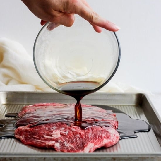 Flank steak marinade being poured over flank steak.