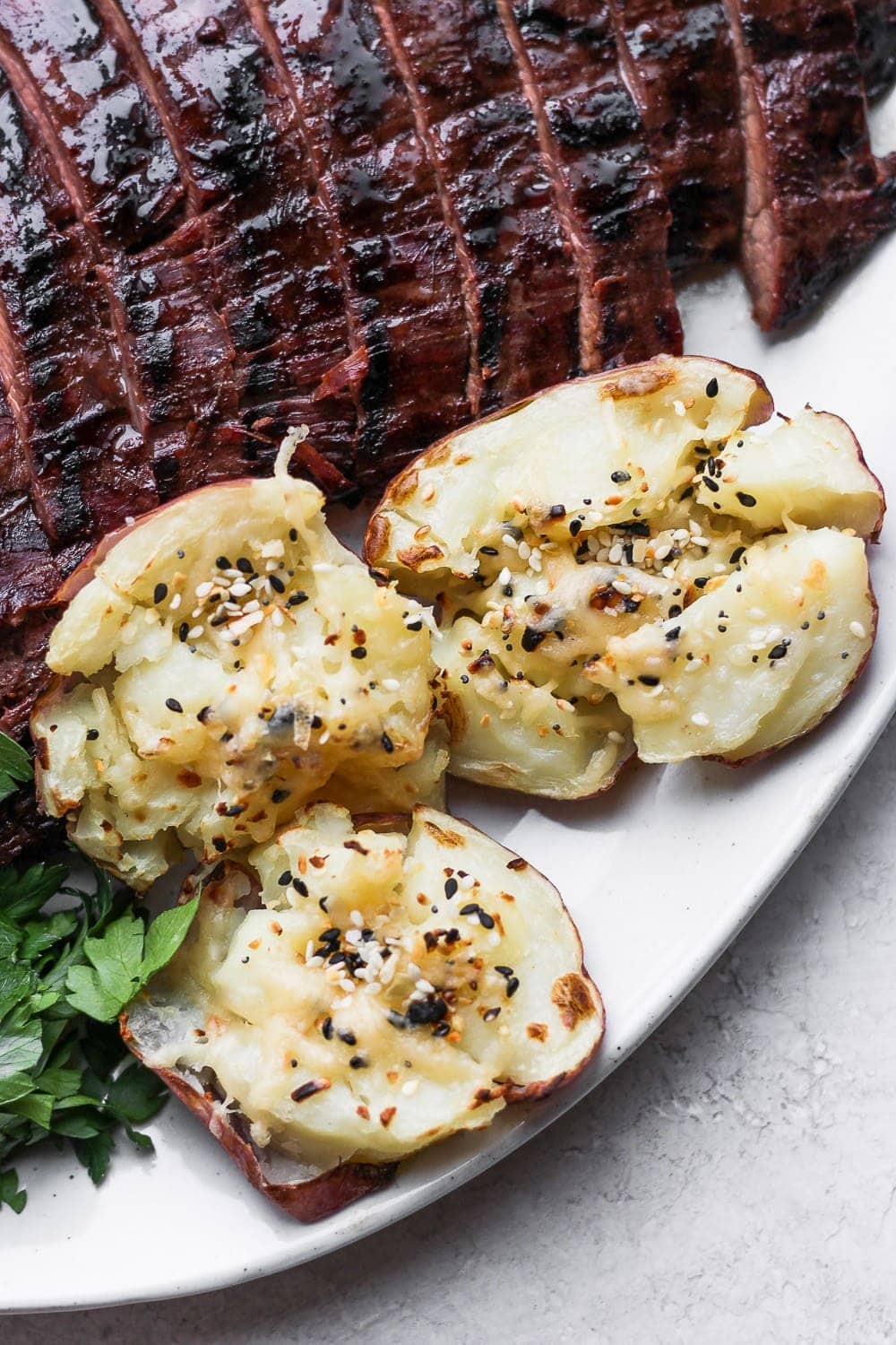 Smashed red potatoes on a plate with flank steak. 