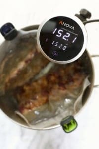 Sous-vide ribs cooking in progress with a digital immersion circulator displaying the water temperature.