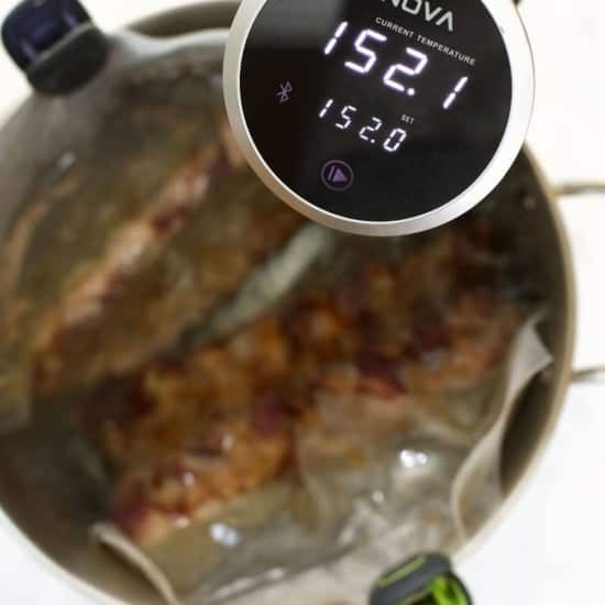 Sous-vide ribs cooking in progress with a digital immersion circulator displaying the water temperature.