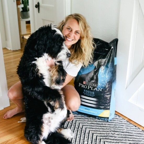 a woman posing with her dog next to a bag of dog food.