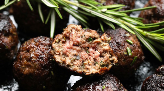 Meatballs with rosemary sprigs on a baking sheet.