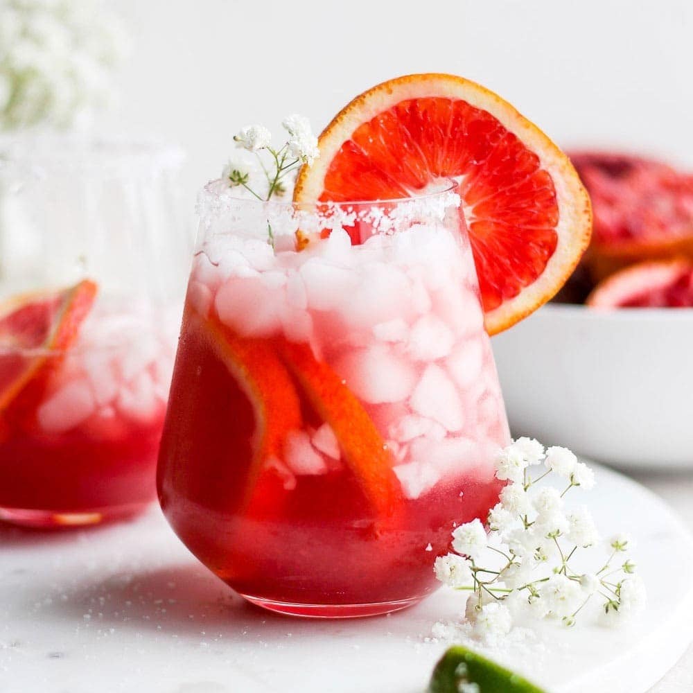 Fit Foodie Finds presents two glasses of grapefruit margarita adorned with ice and flowers.