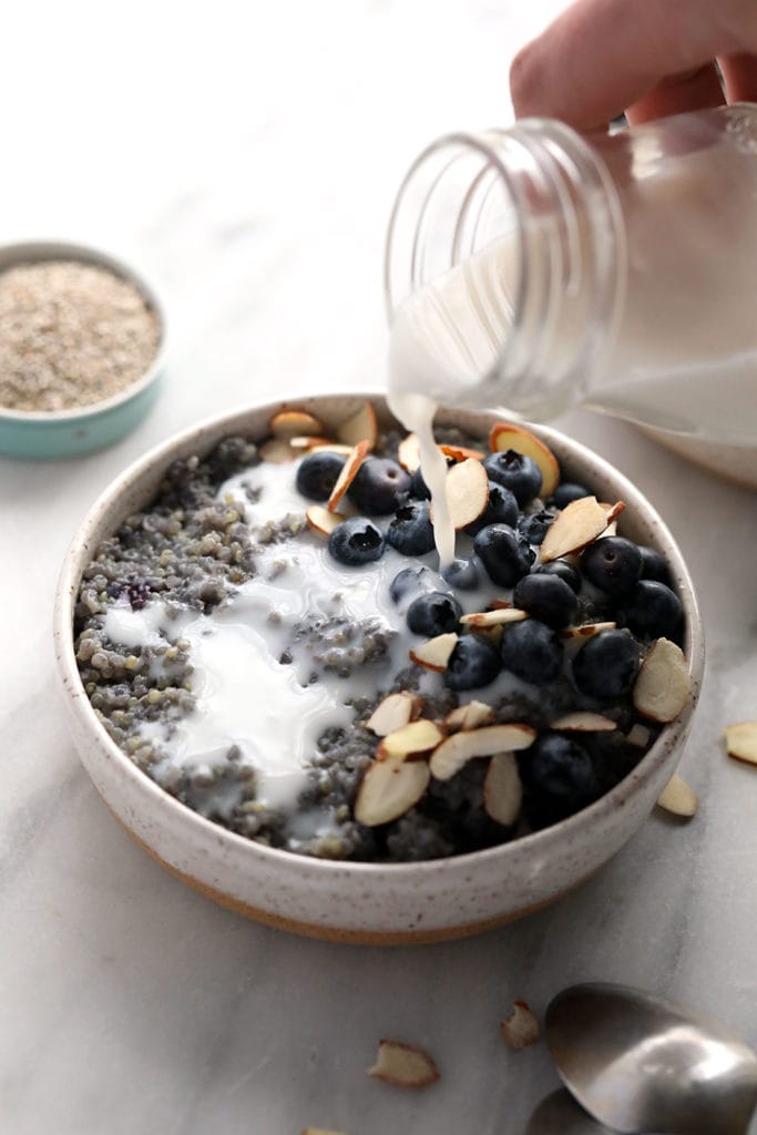 Pouring almond milk over blueberry breakfast quinoa. 