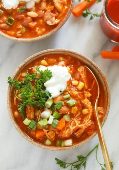 Two bowls of buffalo chicken chili soup with sour cream and carrots.