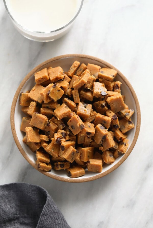 Peanut butter fudge and cookie dough bites in a bowl next to a glass of milk.