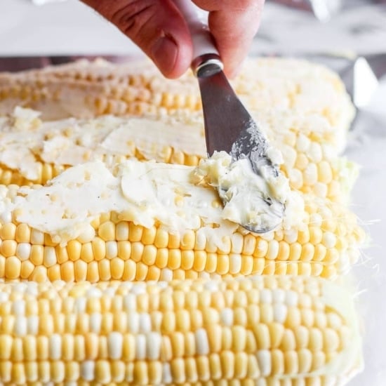a person slicing grilled corn on the cob with a knife.