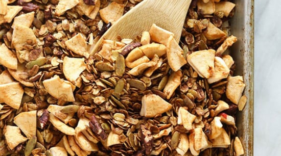 granola on a baking tray being stirred with a spoon