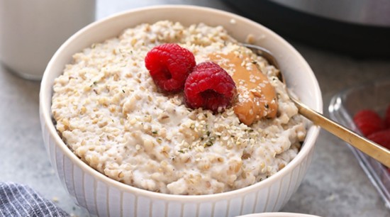 A bowl of oatmeal with raspberries in front of an instant pot.