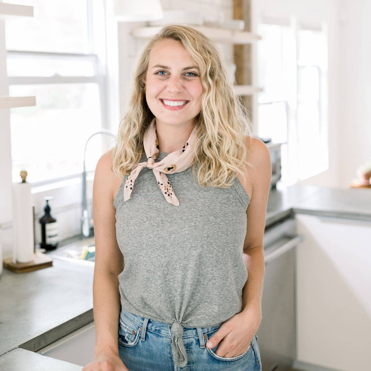 A fit foodie finds a blonde woman in a gray tank top and jeans standing in a kitchen.