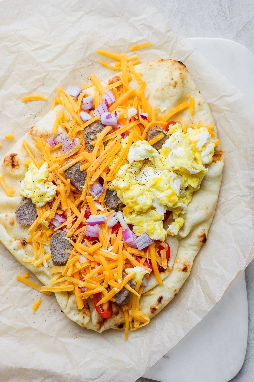 Naan pizza topped with scrambled eggs, cheese, sausage, and onions. 