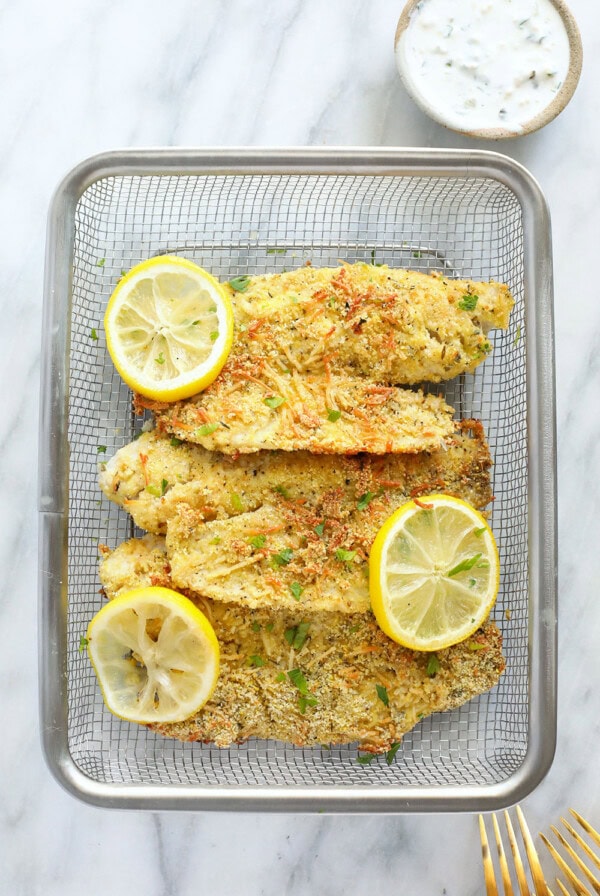 Parmesan crusted tilapia fillets on a plate with lemon wedges.