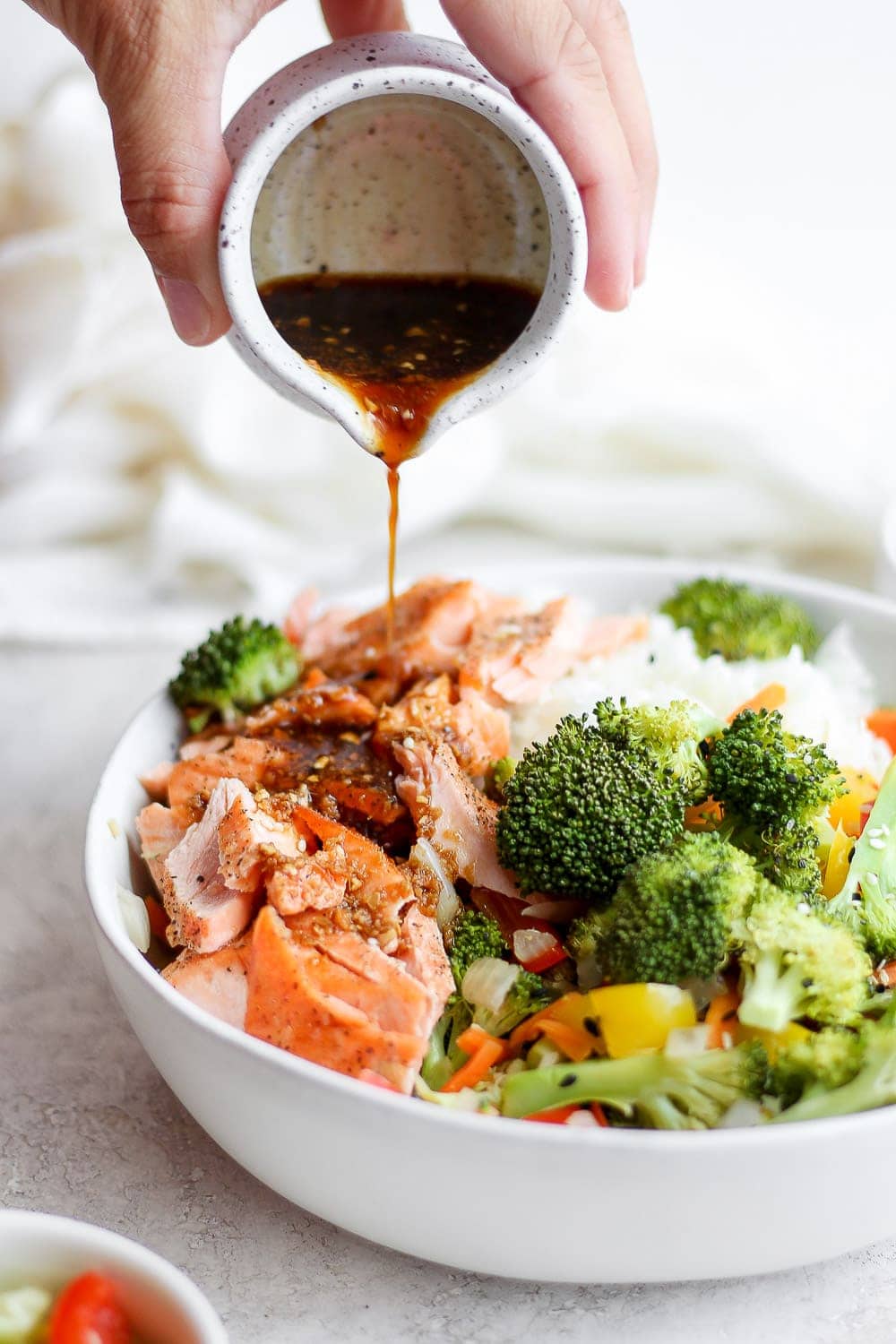 sauce being poured over sheet pan salmon stir fry in a bowl