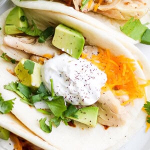 Chicken tacos with sour cream and avocado on a plate.