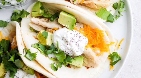 Chicken tacos with sour cream and avocado on a plate.