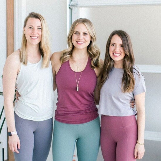 Three fit women pose for a photo in a yoga studio.