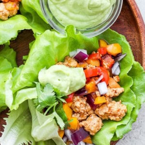 Chicken lettuce wraps with guacamole on a wooden plate.