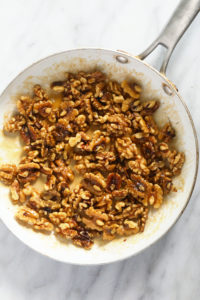 walnuts in a frying pan on a marble countertop.