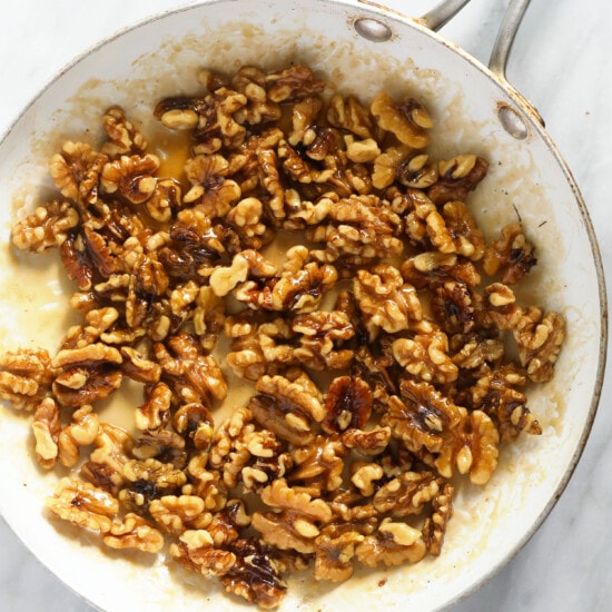 walnuts in a frying pan on a marble countertop.