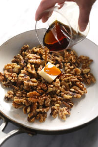 a person pouring syrup over walnuts in a pan.