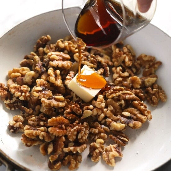 a person pouring syrup over walnuts in a pan.