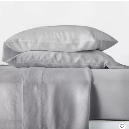 a set of grey sheets and pillows on top of a white bed.