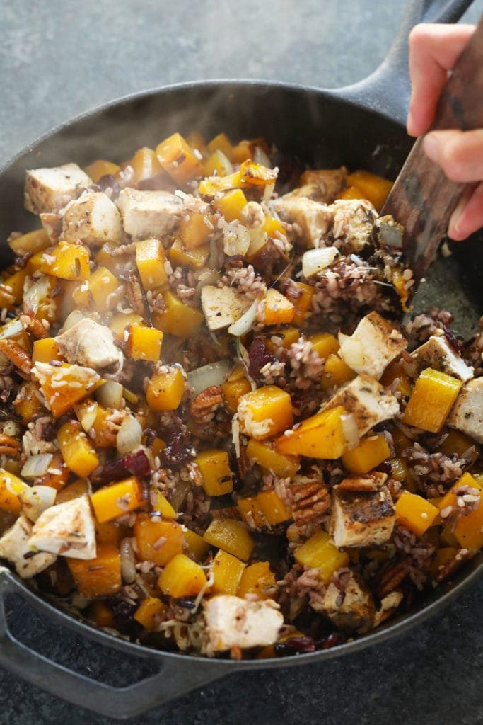 butternut squash wild rice casserole ingredients being mixed together in a cast iron pan