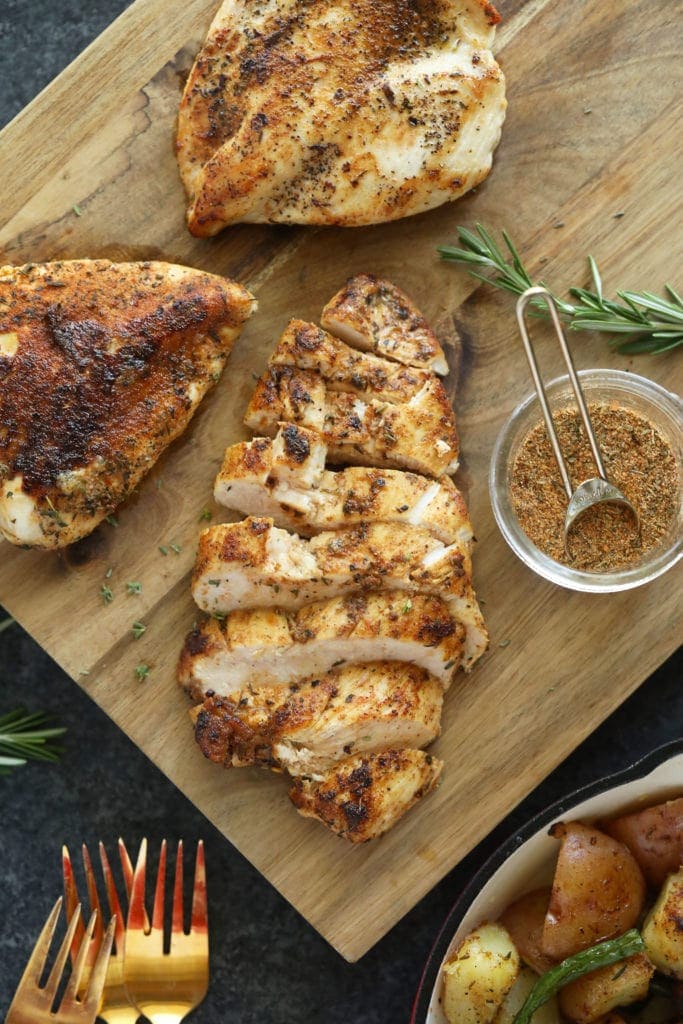 Season and baked chicken breast on a cutting board. 