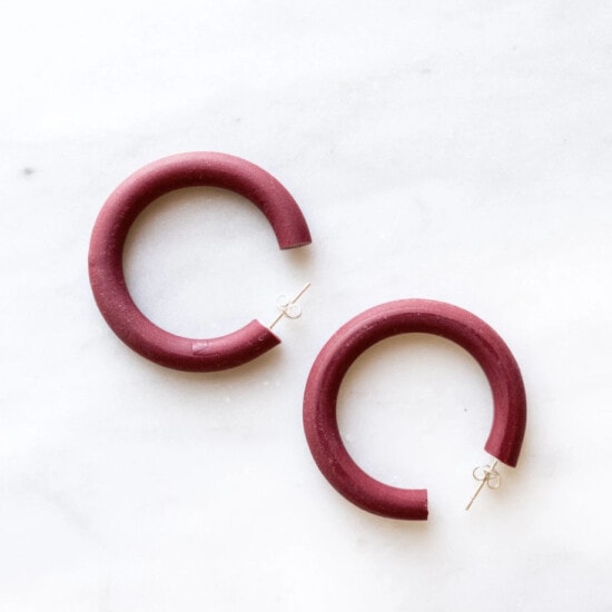 a pair of burgundy hoop earrings on a marble surface.