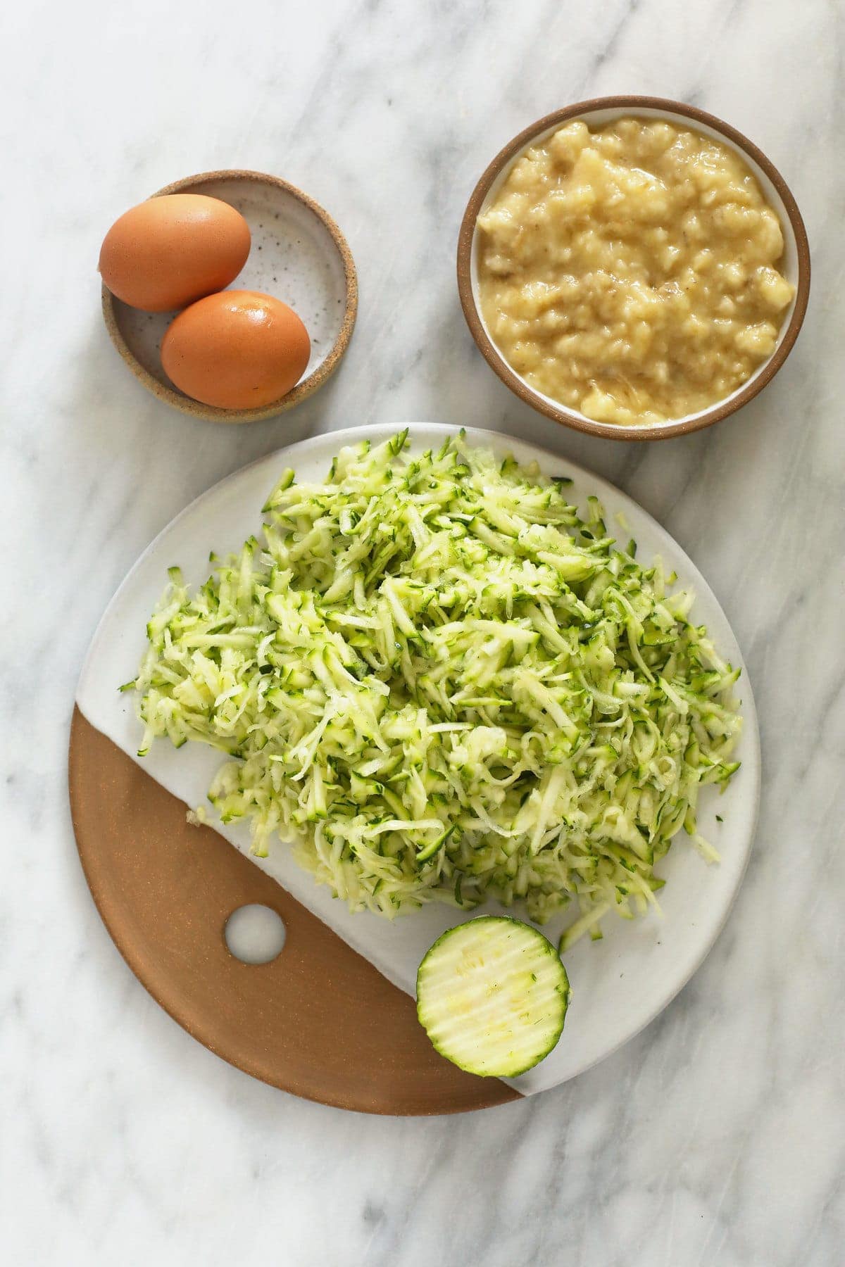 shredded zucchini, eggs, and mashed banana on plates.