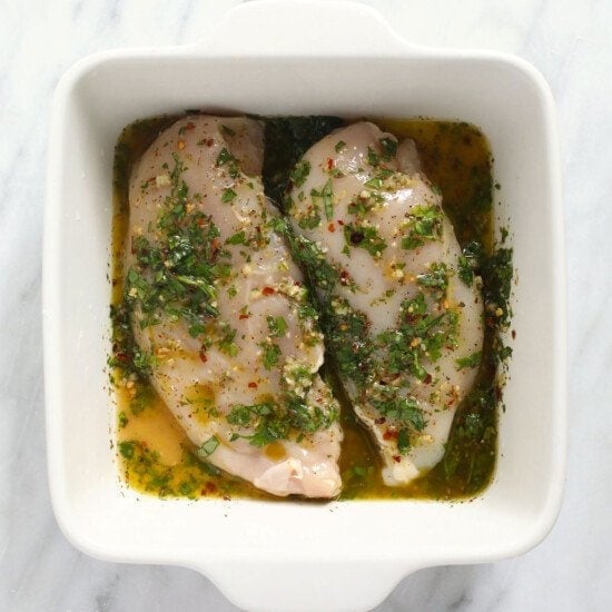 Two Italian chicken breasts in a white dish with herbs.