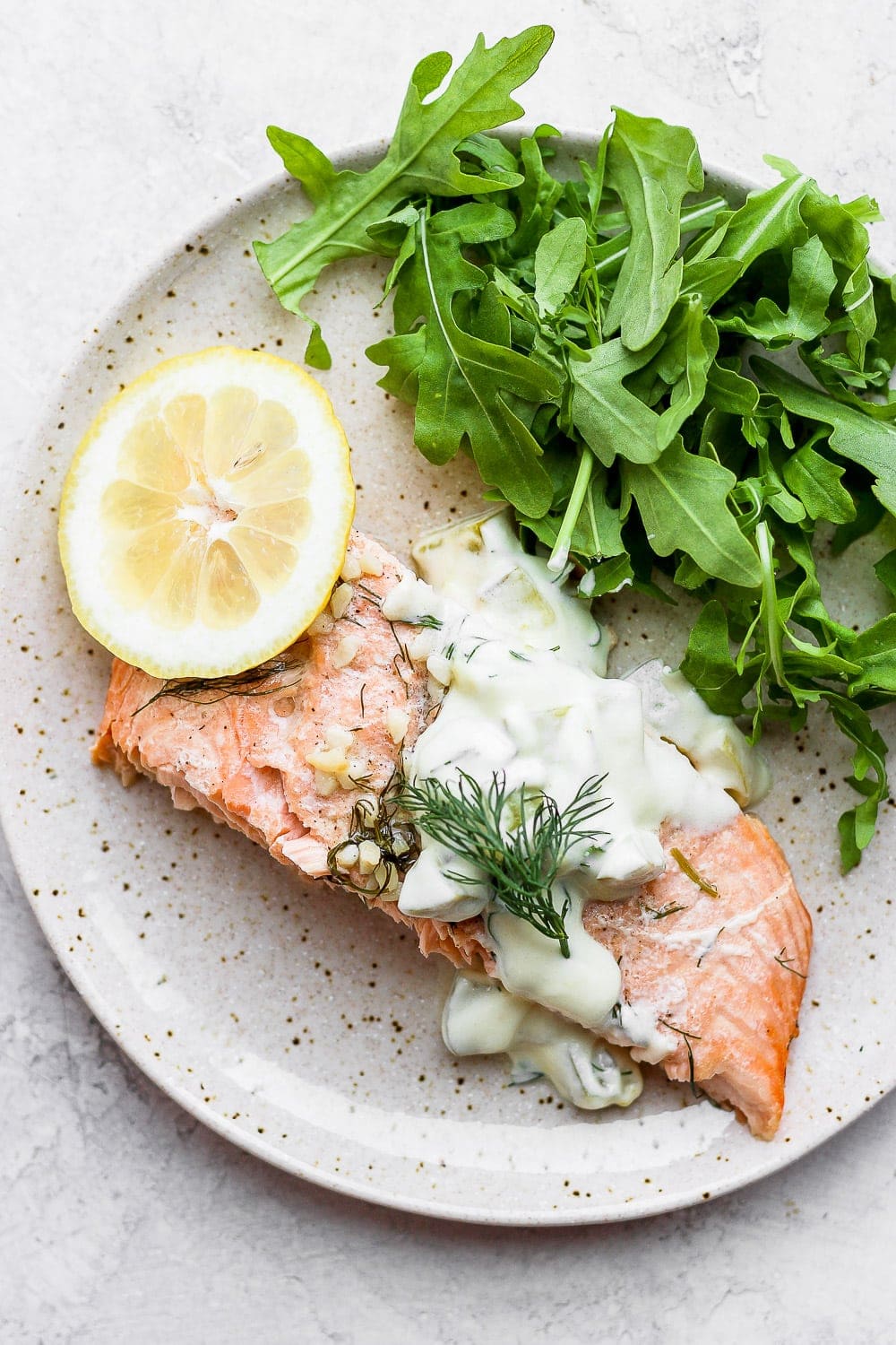 salmon portion on plate with arugula, lemon, and tartar sauce