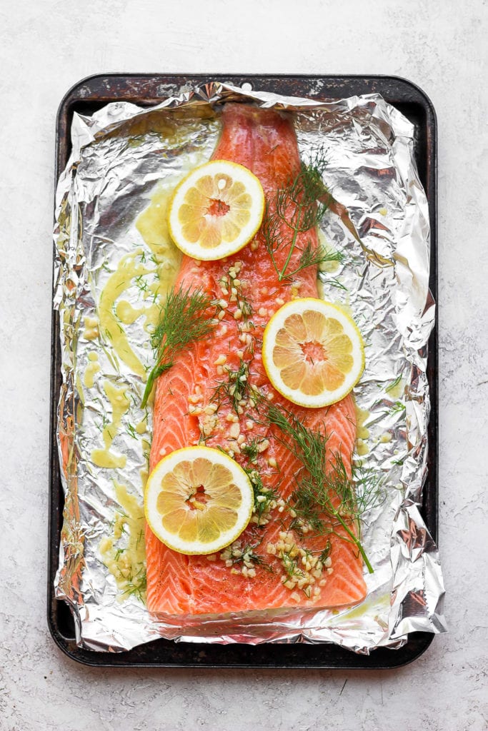 large salmon fillet on tin foil with lemons, dill, and garlic