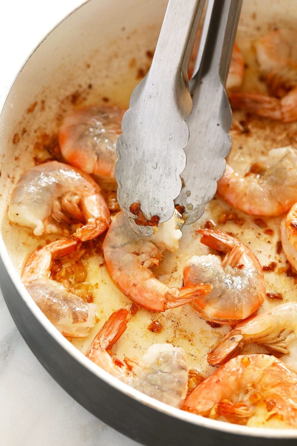 garlic butter shrimp in a skillet being flipped with tongs