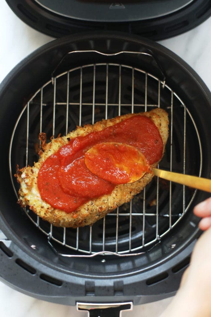 rubbing chicken parmesan with marinara sauce in air fryer