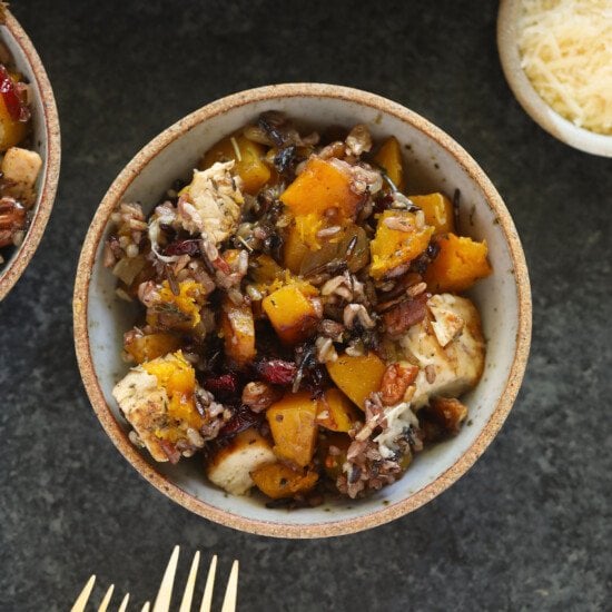Two bowls of butternut squash and chicken wild rice casserole with a fork on a table.