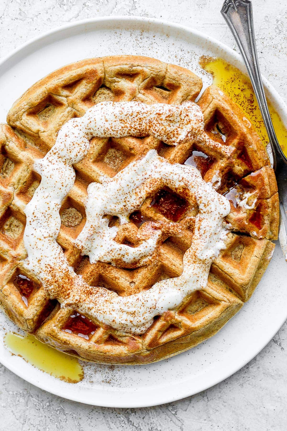 cinnamon roll waffle on a plate with maple syrup and a cream cheese drizzle