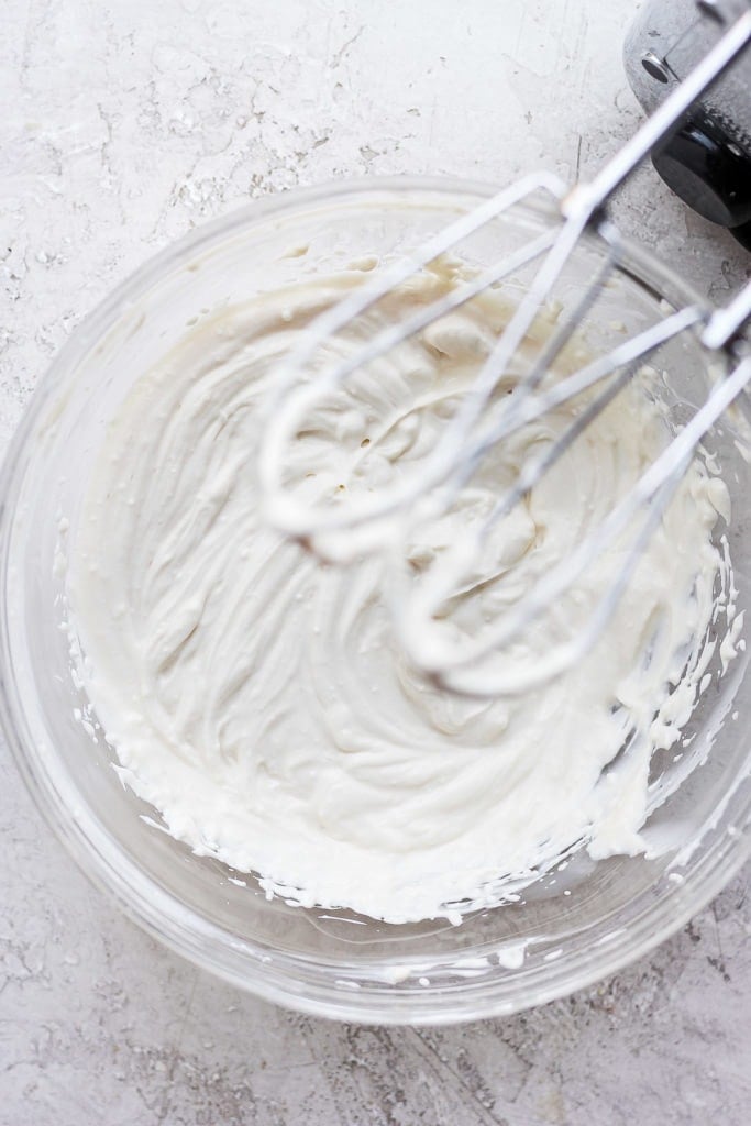 Cream cheese frosting with hand mixer in bowl.