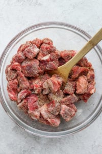 Instant pot shredded beef stew in a glass bowl with a wooden spoon.