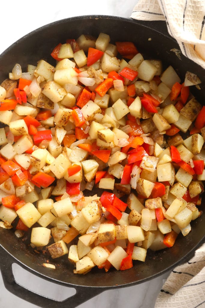 patatas cortadas en cubitos y pimientos rojos en una sartén de hierro fundido