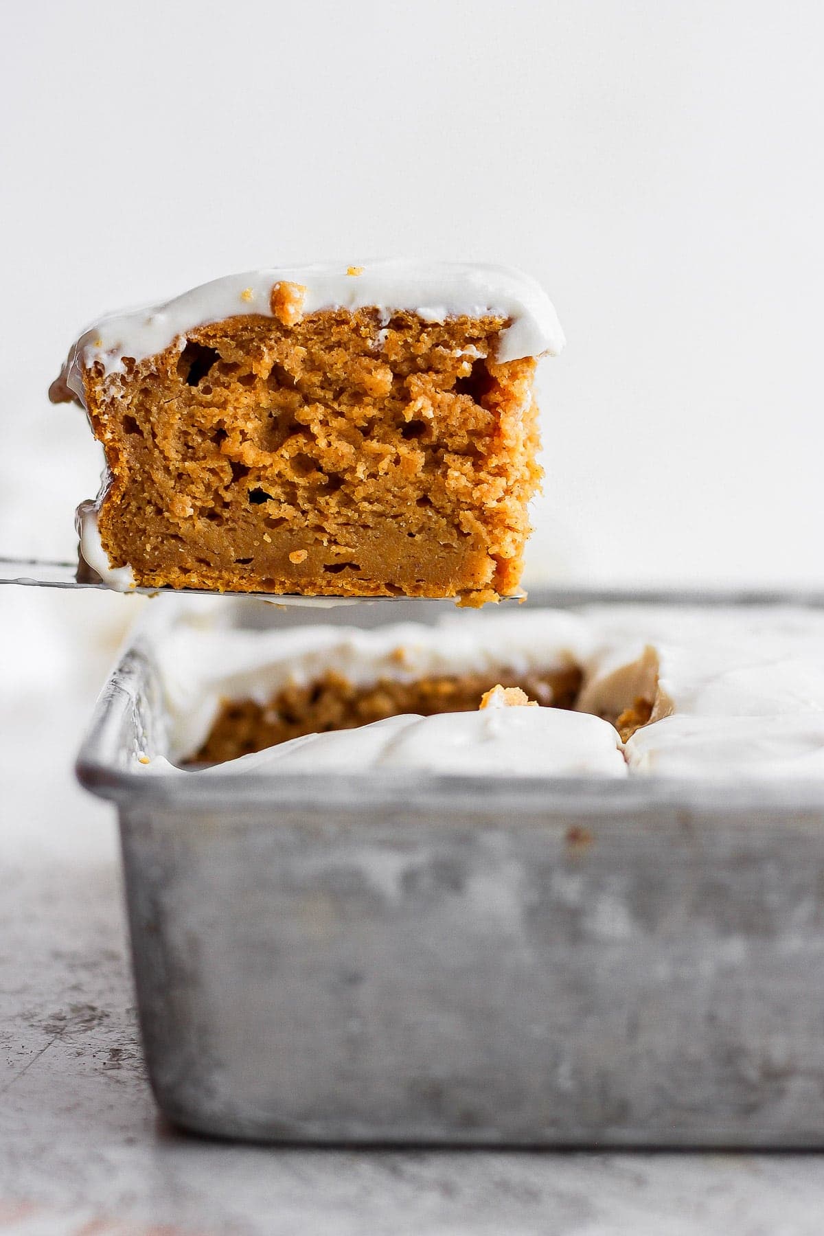 slice of pumpkin sheet cake coming out of the pan