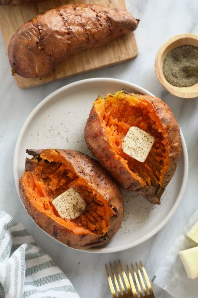 2 sweet potatoes on plate with butter and pepper