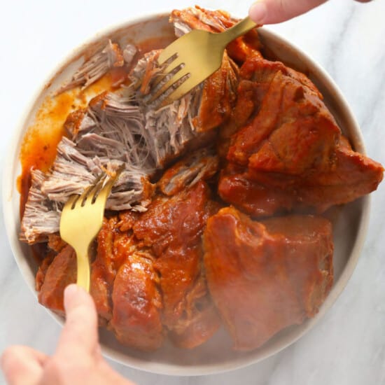 A person holding a fork over a bowl of pulled pork.